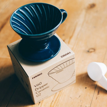 Görseli Galeri görüntüleyiciye yükleyin, İndigo Mavisi Hario V60 02 seramik dripper, ürün kutusu ve ölçü kaşığıyla ahşap masada
