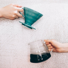 Görseli Galeri görüntüleyiciye yükleyin, Turkuaz Yeşili Hario V60 02 seramik dripper ve kahve dolu cam sunucu elde tutulurken

